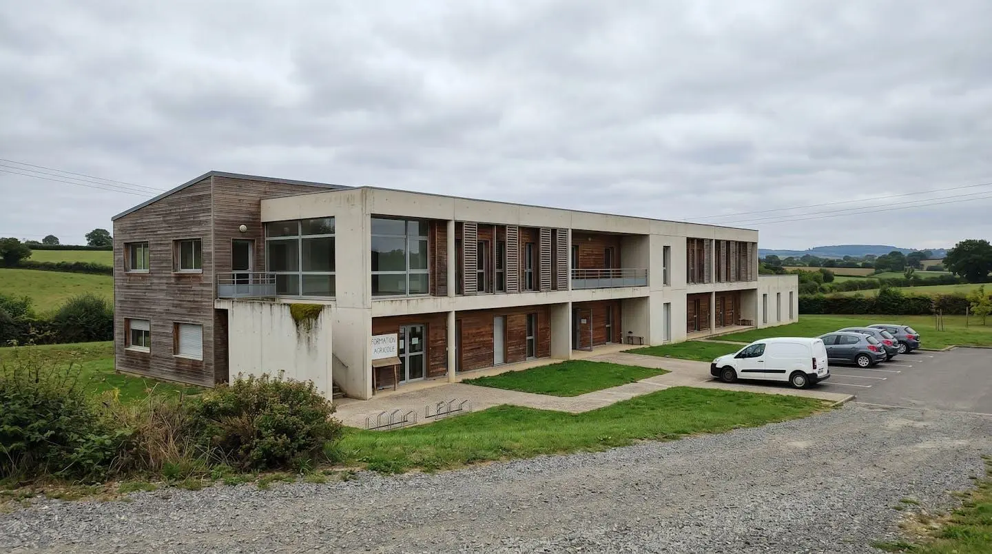 Vue en angle large d'un bâtiment éducatif moderne avec une façade claire entourée d'espaces verts et d'arbres sous un ciel bleu lumineux